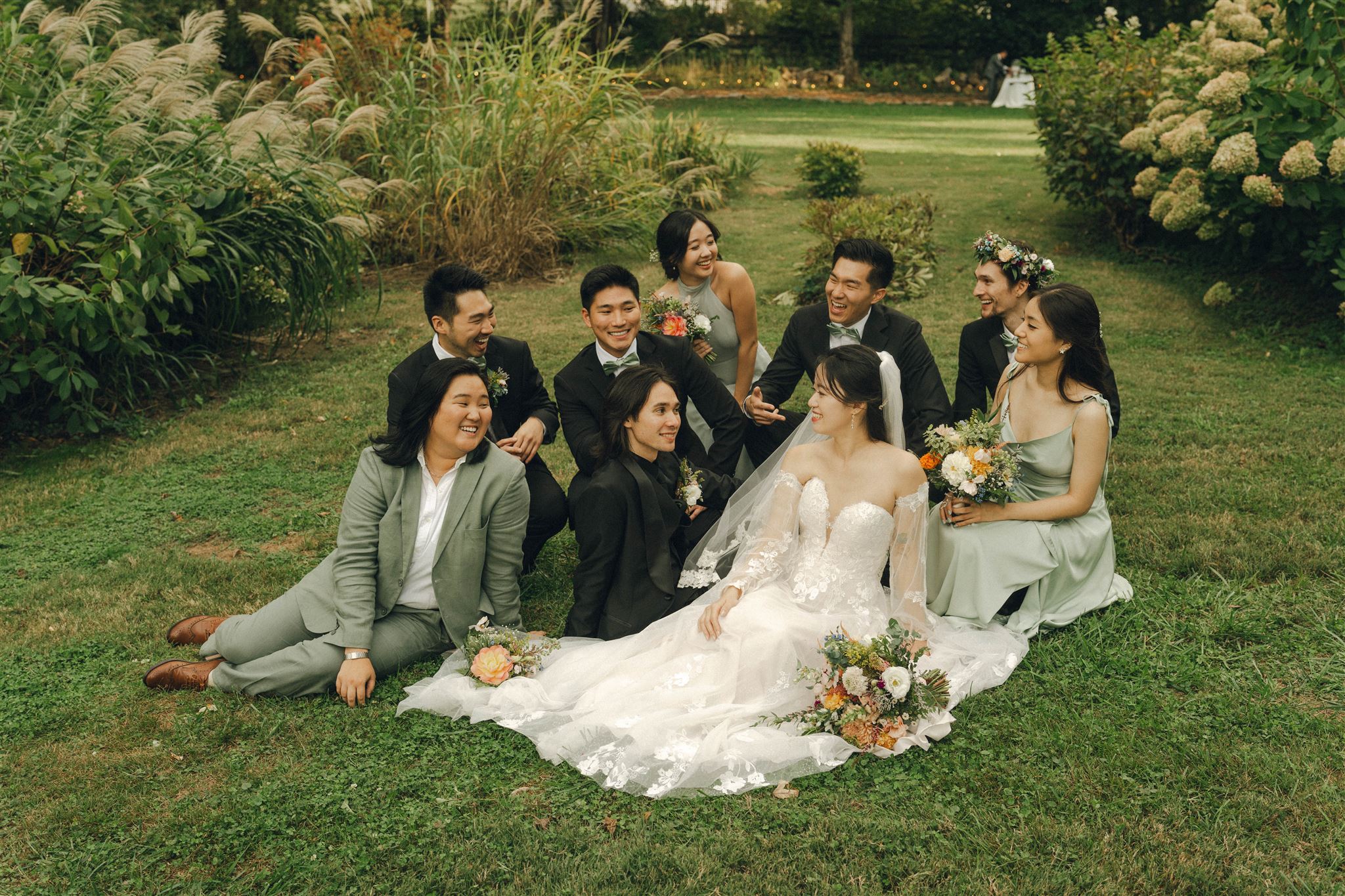 Whimsical secret garden wedding with bridal party sitting on the grass together while laughing